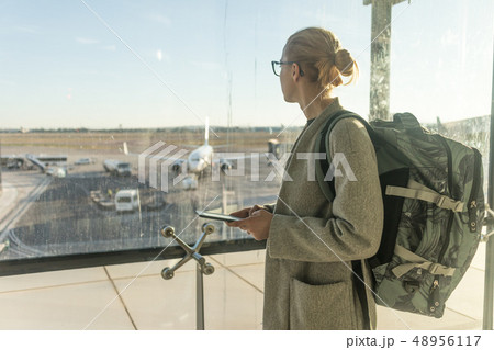 Casually dressed female traveler at airport, holding smart phone device, looking through the airport Casually dressed female traveler at airport, holding smart phone device, looking through the airport 48956117