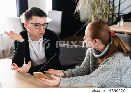 Girlfriend asking for explanation of her boyfriend sitting on a couch in the cafe 48962204