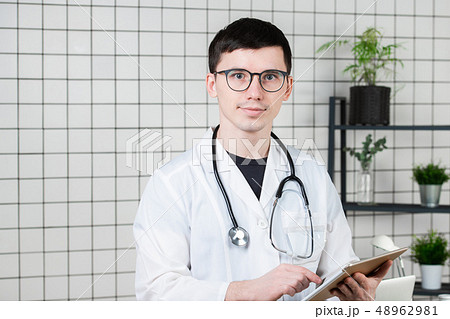 Pensive handsome young male doctor using tablet computer. Technologies in medicine concept Pensive handsome young male doctor using tablet computer. Technologies in medicine concept 48962981