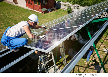 Professional worker installing solar panels on the green metal construction Professional worker installing solar panels on the green metal construction 48963399