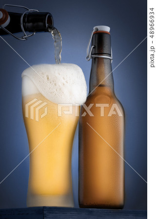The glass is poured cold beer and a bottle of beer close-up on a blue background. Foam over the edge The glass is poured cold beer and a bottle of beer close-up on a blue background. Foam over the edge 48966934
