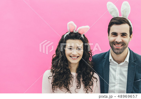Young pretty pair standing on pink background. At the same time stands next to his wife. Sincerely 48969657