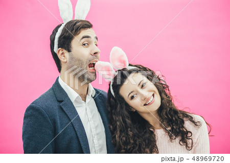 Young happy couple standing on pink background. With a bunny ears on the head. The girl put her head Young happy couple standing on pink background. With a bunny ears on the head. The girl put her head 48969720