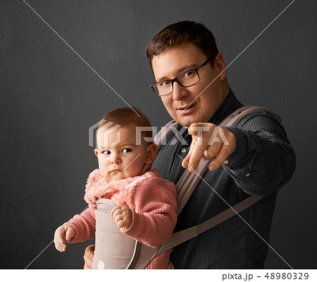 Fathre and his kid in baby carrier at the grey background wall, baby wearing concept Fathre and his kid in baby carrier at the grey background wall, baby wearing concept 48980329