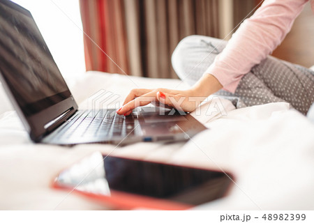 Female person drinks coffee and uses laptop in bed 48982399