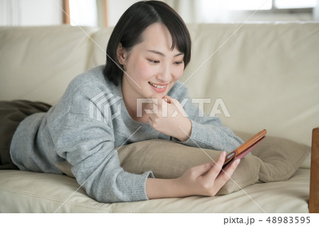 ソファに寝転んでスマホを見る若い日本人女性 48983595