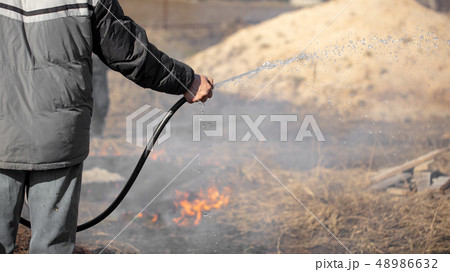 A man extinguishes the burning grass with water A man extinguishes the burning grass with water 48986632