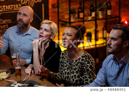 Group of friends watching tv in a cafe behind bar counter Group of friends watching tv in a cafe behind bar counter 48988401