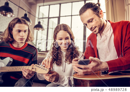 Beaming curly girl feeling joyful while learning to play guitar 48989728