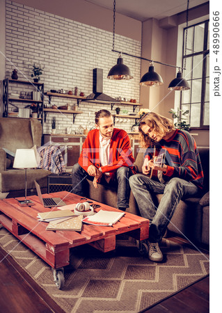 Student wearing jeans and sweater playing the guitar near tutor 48990666
