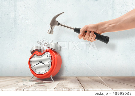 A man's hand holding a hammer and crashing a retro alarm clock standing on the wooden floor. A man's hand holding a hammer and crashing a retro alarm clock standing on the wooden floor. 48995035