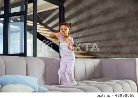 Amazing curly-haired girl jumping alone on sofa 48998069
