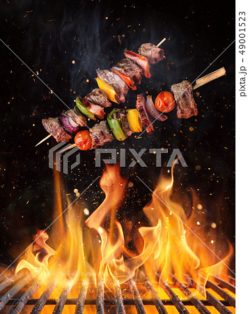Tasty skewers flying above cast iron grate with fire flames. 49001523