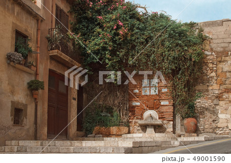 old Spanish house decorated with a flowering tree, near an ancient faucet and water bowl 49001590