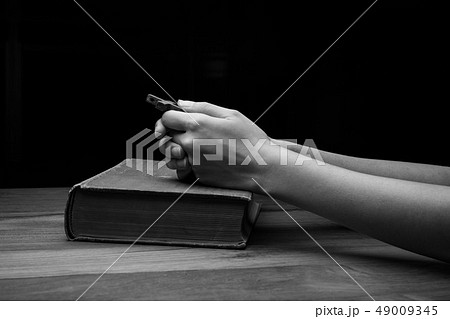 Hands folded in prayer over Holy Bible 49009345