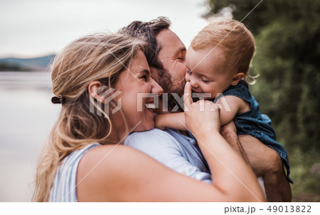 A young family with a toddler girl outdoors by the river in summer. 49013822