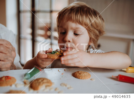 A small toddler boy sitting at the table, decorating and eating cakes at home. A small toddler boy sitting at the table, decorating and eating cakes at home. 49014635