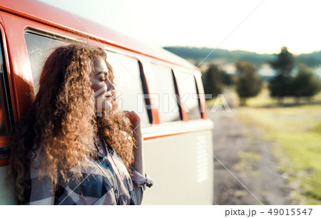 A young girl on a roadtrip through countryside, leaning on a minivan. 49015547