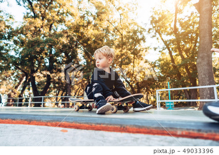 Young kid sitting in the park on a skateboard. Young kid sitting in the park on a skateboard. 49033396