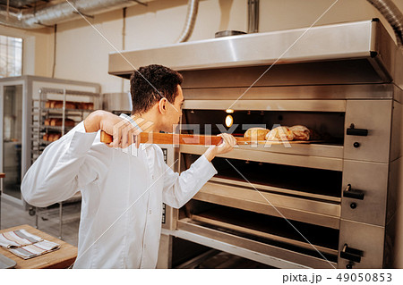 Young baker taking ready bread out of big oven in the kitchen 49050853