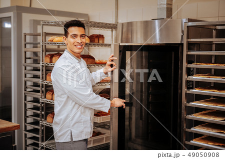 Pleasant baker standing near big oven in the kitchen 49050908