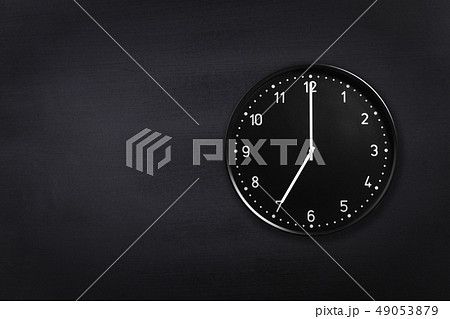 Wall clock showing seven o'clock on black chalkboard background. Office clock showing 7am or 7pm on 49053879