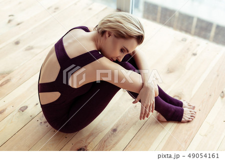 Short-haired woman in violet outfit grabbing her foot with both hands 49054161