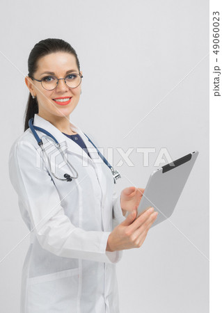 Portrait of brunet in doctors costume with a modern tablet in her hands isolated on background Portrait of brunet in doctors costume with a modern tablet in her hands isolated on background 49060023