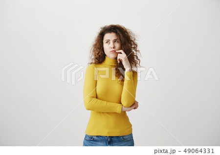 Portrait of young tricky woman touching lock of hair meaning she has something in mind with facial Portrait of young tricky woman touching lock of hair meaning she has something in mind with facial 49064331