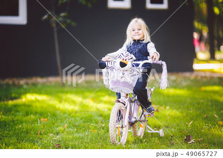 Funny child Caucasian girl blonde near a purple bike with a basket and a zebra toy in an outside 49065727
