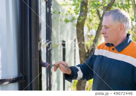 worker painting black metal fence pipe with  brush 49072446