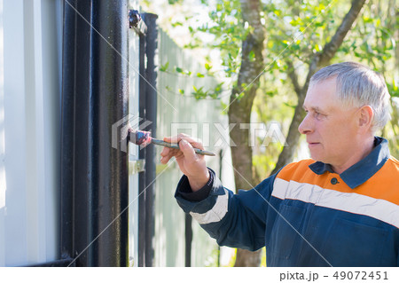 worker painting black metal fence pipe with  brush 49072451