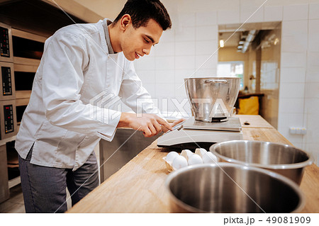 Baker wearing white jacket using modern kitchen scales Baker wearing white jacket using modern kitchen scales 49081909