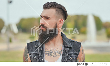 Portrait of a brutal and bearded man with tattoos on his shoulders. Portrait of a brutal and bearded man with tattoos on his shoulders. 49083369