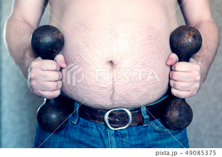 A man with a big belly holds sport dumbbells. 49085375