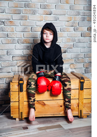Little boy boxer with blonde hair dressing in black sweatshirt wearing boxing gloves posing in a 49104894