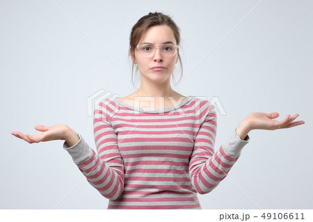 Puzzled young woman  shrugs shoulders 49106611