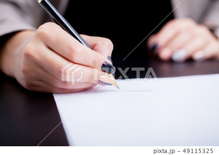 Close up girl hand putting signature on document. She situating at desk. Business concept. Low angle Close up girl hand putting signature on document. She situating at desk. Business concept. Low angle 49115325