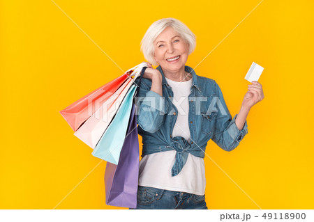 Senior woman shopper studio isolated on yellow wall carry bags holding credit card 49118900