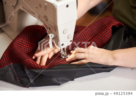 Female hands at sewing process and repairing plaid fabric on professional manufacturing machine 49125394