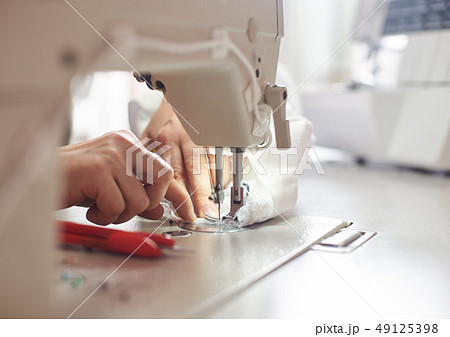 Female hands at sewing process and repairing white fabric on professional manufacturing machine Female hands at sewing process and repairing white fabric on professional manufacturing machine 49125398