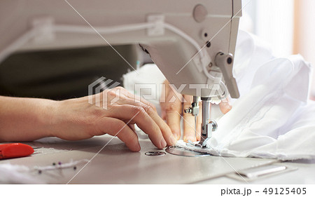 Female hands at sewing process and repairing white fabric on professional manufacturing machine 49125405