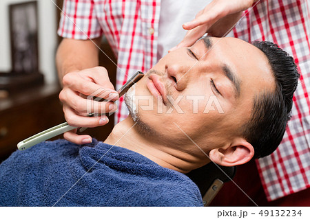 Barber shaving with straight razor 49132234