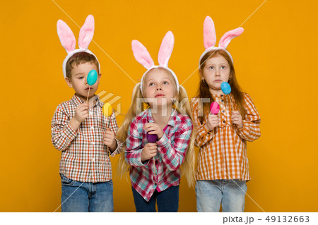 two little girls and boy with Easter bunny ears holding colorful eggs two little girls and boy with Easter bunny ears holding colorful eggs 49132663