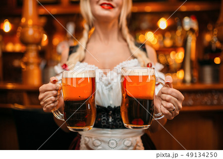 Sexy waitress holds two mugs of fresh beer in pub 49134250