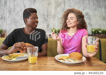 Young woman and man eating hamburgers, french fries in cafe. Young woman and man eating hamburgers, french fries in cafe. 49160220