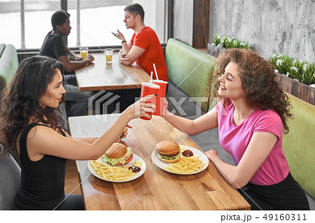 Happy girls sitting in fast food cafe, clinking paper cups. Happy girls sitting in fast food cafe, clinking paper cups. 49160311