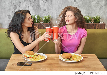 Pretty girls sitting in cafe and clinking paper cups. Pretty girls sitting in cafe and clinking paper cups. 49160325