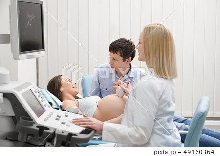 Pregnant woman with husband on ultrasound exam. Pregnant woman with husband on ultrasound exam. 49160364