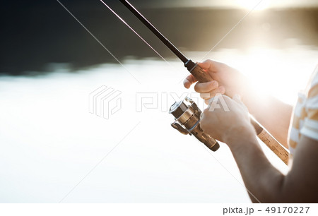 Midsection of a man fishing by a lake, holding a rod. A close-up. 49170227